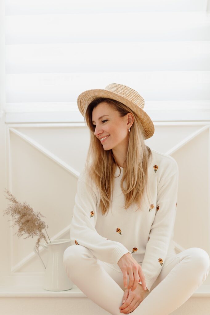 A young woman is smiling in a summer hat in white room. Boho