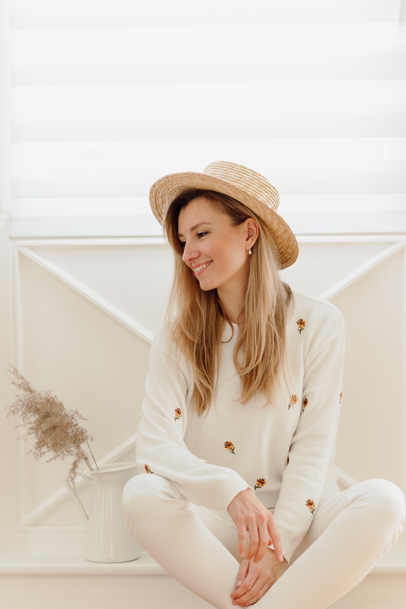 A young woman is smiling in a summer hat in white room. Boho